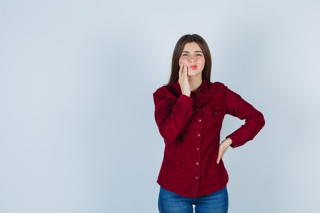 Retrato de niña que sufre de dolor de muelas en blusa burdeos y parece doloroso