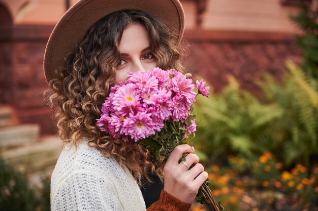 Retrato de niña rizada con ramo de flores cerca de la cara