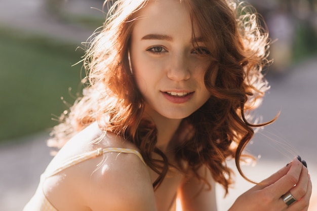 Retrato de niña romántica jengibre posando con una sonrisa suave en la naturaleza borrosa. Feliz mujer pelirroja mirando en la soleada mañana de verano.