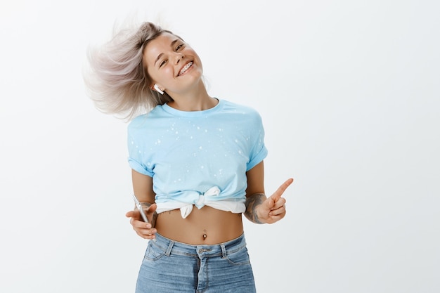 Retrato de niña rubia despreocupada posando en el estudio con su teléfono y auriculares