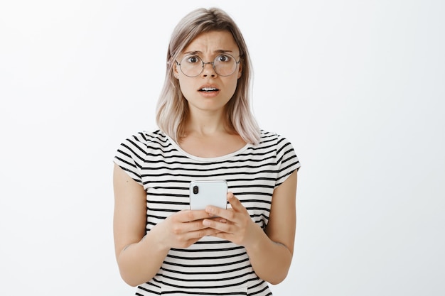 Retrato de niña rubia frustrada posando en el estudio con su teléfono