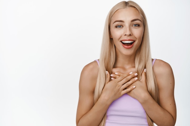 Foto gratuita retrato de niña rubia jadeando asombrado, mirando sorprendido, halagado y tocado, de pie sobre blanco