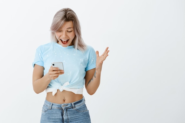 Retrato de niña rubia satisfecha posando con su teléfono en el estudio