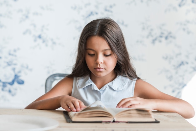 Retrato de una niña sentada frente a papel tapiz leyendo libro