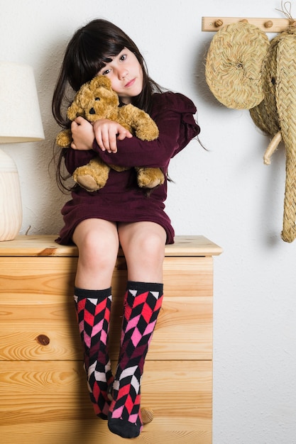 Retrato de una niña sentada en la mesa con juguetes de peluche