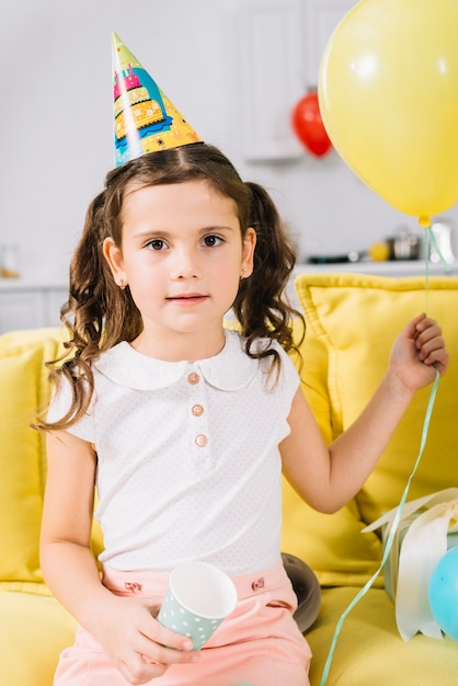 Retrato de una niña sentada en el sofá sosteniendo el globo en la mano