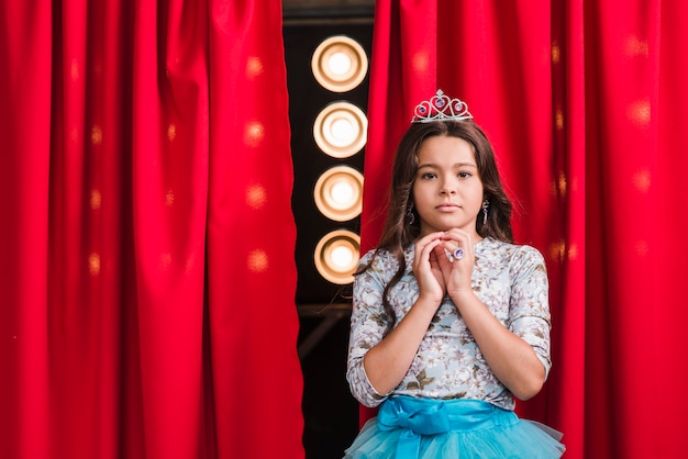 Retrato de niña seria de pie delante de la cortina roja con luz de la etapa