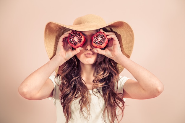 Retrato de una niña en un sombrero de verano con fruta en una pared de color