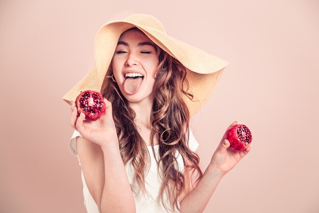 Retrato de una niña en un sombrero de verano con fruta en una pared de color