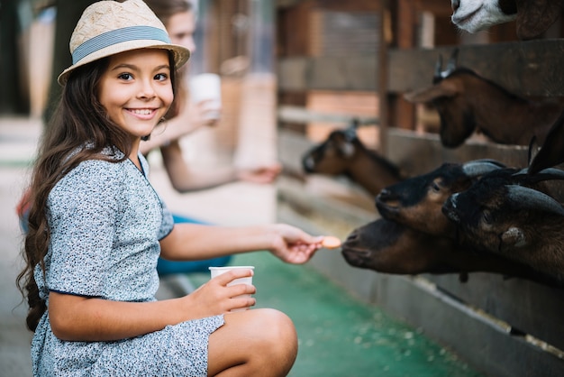 Retrato de niña sonriente alimentación galleta a cabra en el granero