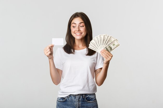 Retrato de niña sonriente emocionada con dinero y tarjeta de crédito, blanco.