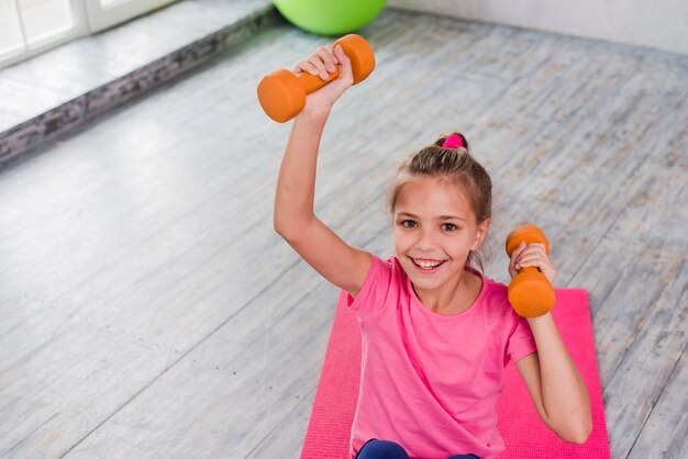 Retrato de una niña sonriente haciendo ejercicio con una pesa de gimnasia naranja