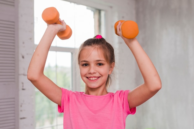 Retrato de una niña sonriente haciendo ejercicio con una pesa de gimnasia naranja