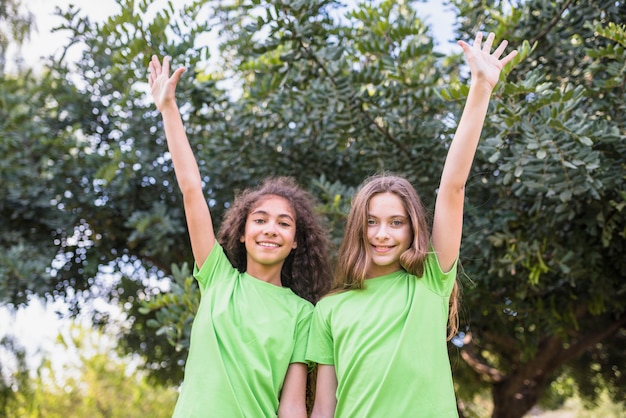 Foto gratuita retrato de una niña sonriente levantando su brazo de pie delante de los árboles