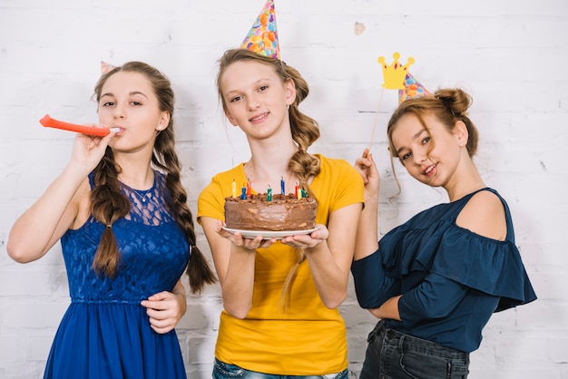 Retrato de una niña sonriente con pastel de cumpleaños de pie con sus amigos