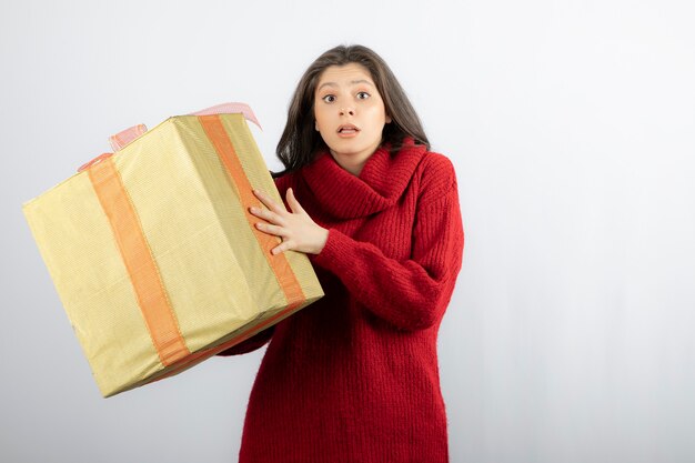 Retrato de una niña sorprendida sosteniendo una caja de regalo aislada sobre una pared blanca.