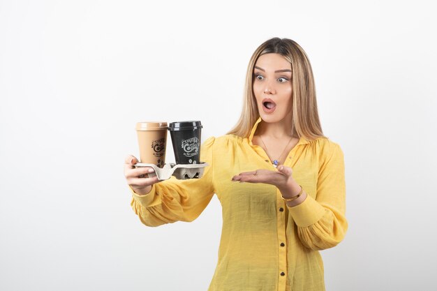 Retrato de niña sorprendida sosteniendo tazas de café y de pie sobre blanco.
