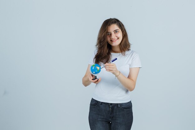 Retrato de niña sosteniendo bolígrafo en globo en camiseta, jeans y mirando feliz vista frontal