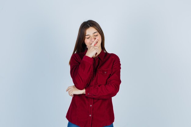 Foto gratuita retrato de niña sosteniendo la mano en la barbilla, cerrando los ojos en camisa casual y mirando avergonzado