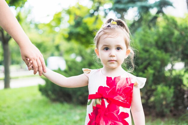 Retrato de una niña sosteniendo las manos de la persona en el jardín