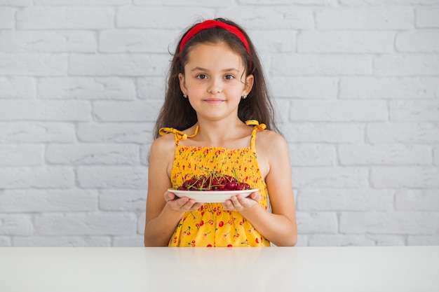 Retrato de una niña sosteniendo un plato de cerezas rojas