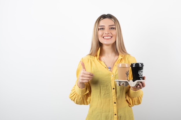 Retrato de niña sosteniendo tazas de café y dando pulgares.