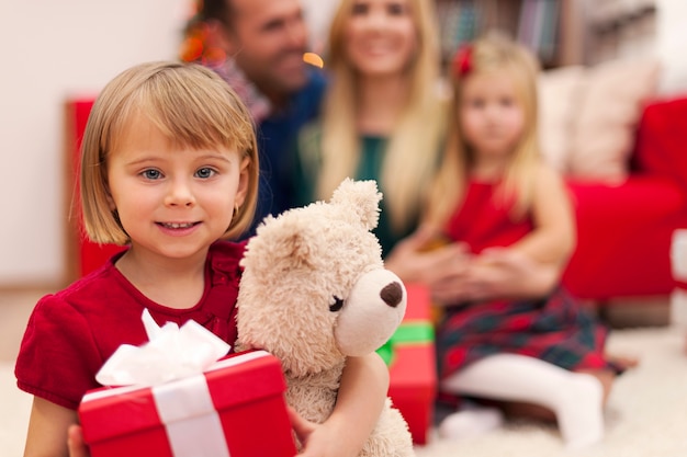 Retrato de niña con su osito de peluche y su familia en Navidad