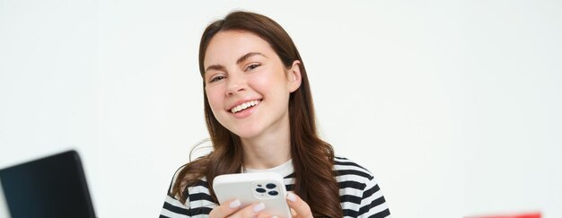 Foto gratuita retrato de una niña con un teléfono inteligente riéndose usando una aplicación de teléfono móvil aislada sobre fondo blanco