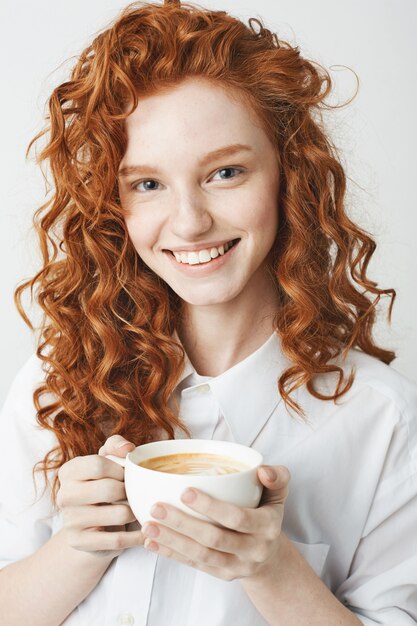 Retrato de niña tierna pelirroja con pecas sonriendo sosteniendo la taza