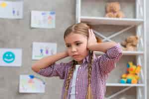 Foto gratuita retrato de niña triste cubriendo sus orejas con dos manos