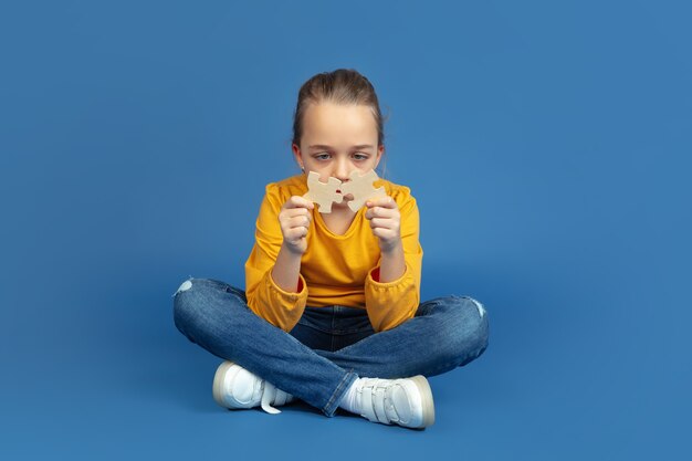 Retrato de niña triste sentada aislada sobre fondo azul de estudio. Cómo se siente ser autista. Problemas modernos, nueva visión de los problemas sociales. Concepto de autismo, infancia, salud, medicina.
