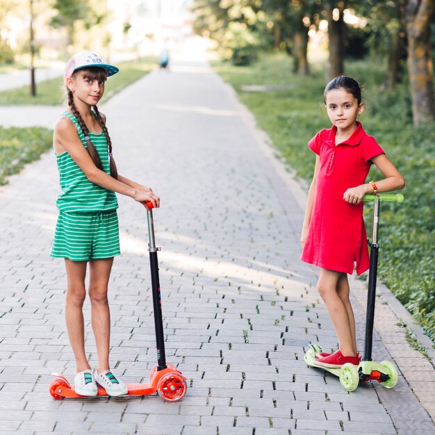 Retrato de niñas de pie en patinete scooter en el parque