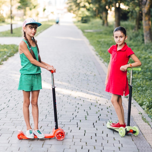 Retrato de niñas de pie en patinete scooter en el parque