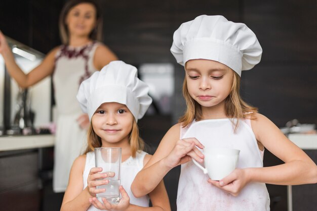Retrato de niñas con sombrero de chef con vaso y taza