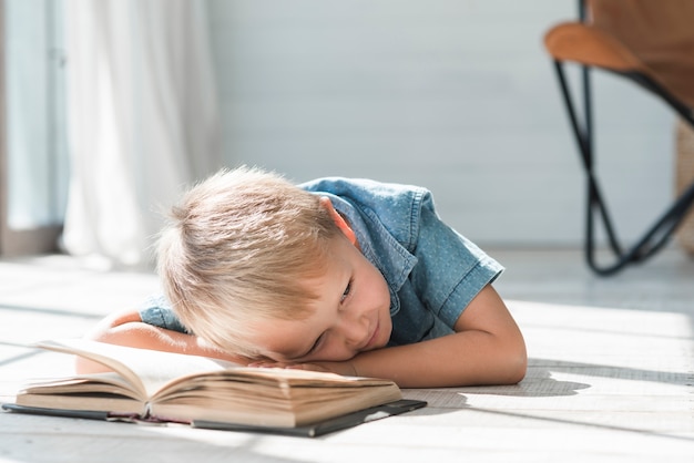 Retrato de niño acostado en el piso con un libro abierto en casa