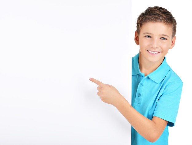 Foto gratuita retrato de niño alegre apuntando en cartel blanco aislado en blanco