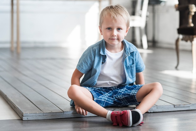 Retrato de un niño bonito sentado en el piso de madera en casa
