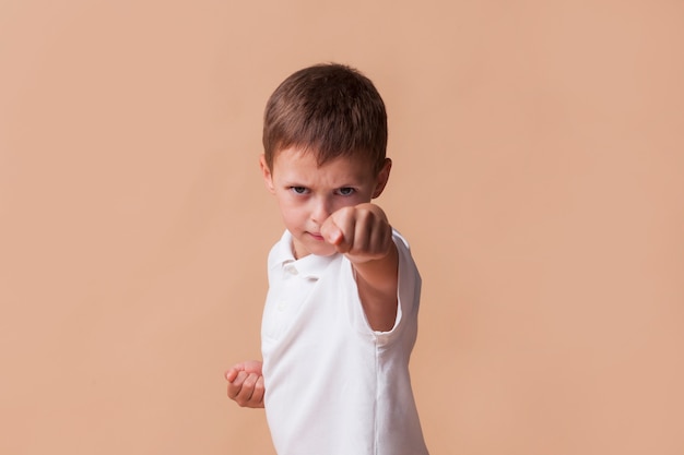 Retrato de niño cerrando el puño para pelear sobre fondo beige