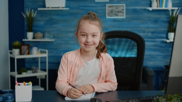 Retrato de niño haciendo los deberes en el portátil para la educación en el escritorio con la computadora. niña con lápiz, preparándose para la lección de clase en línea remota en casa. alumno aprendiendo para el conocimiento