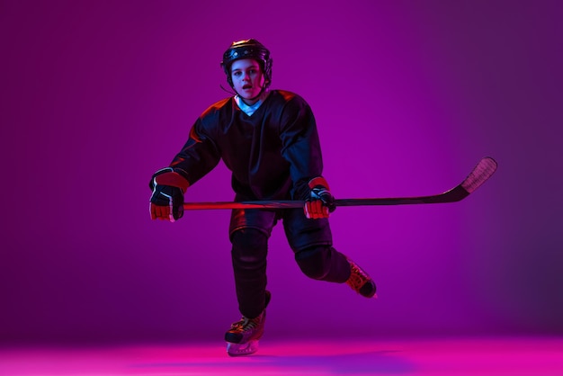 Retrato de niño jugador de hockey entrenamiento aislado sobre fondo púrpura en neón