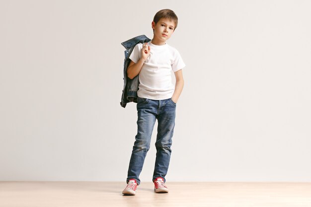 El retrato de niño lindo en ropa de jeans con estilo mirando a la cámara en el estudio
