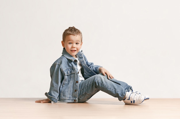 Foto gratuita el retrato de niño lindo en ropa de jeans con estilo mirando a la cámara en el estudio