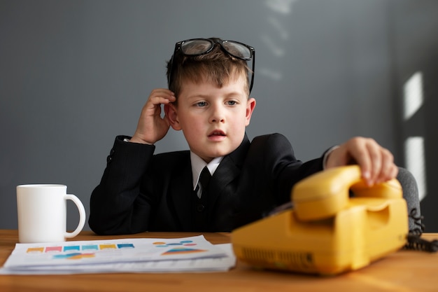 Retrato de niño lindo en traje usando teléfono rotatorio en la oficina