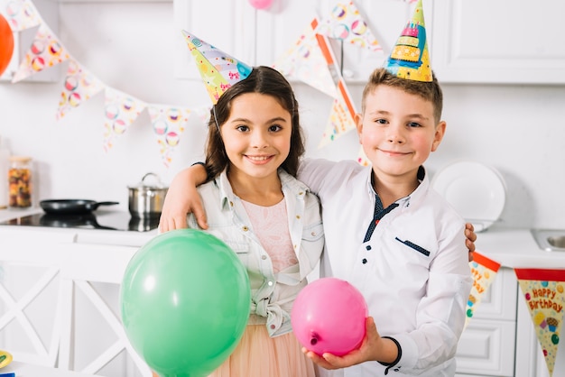 Foto gratuita retrato de niño y niña con globos de pie en la cocina