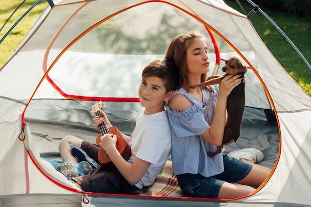 Retrato de un niño y una niña sentados en una tienda de campaña con un perro y un ukelele.