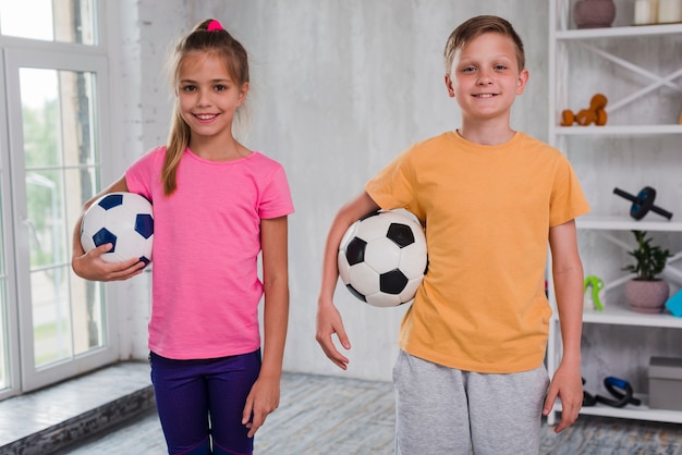 Retrato de un niño y una niña sonrientes que sostienen el balón de fútbol que mira la cámara