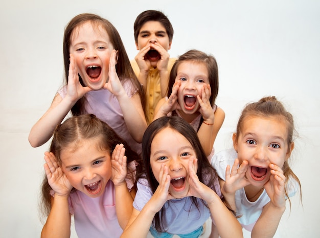 El retrato de niño y niñas felices lindos niños pequeños en ropa casual elegante mirando al frente contra la pared blanca del estudio