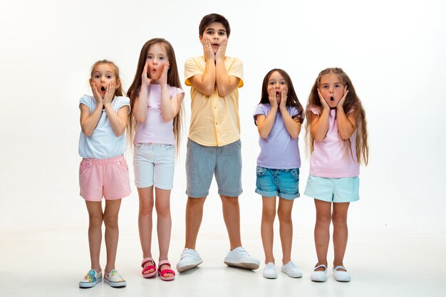 El retrato de niño y niñas felices lindos niños pequeños en ropa casual elegante mirando al frente contra la pared blanca del estudio