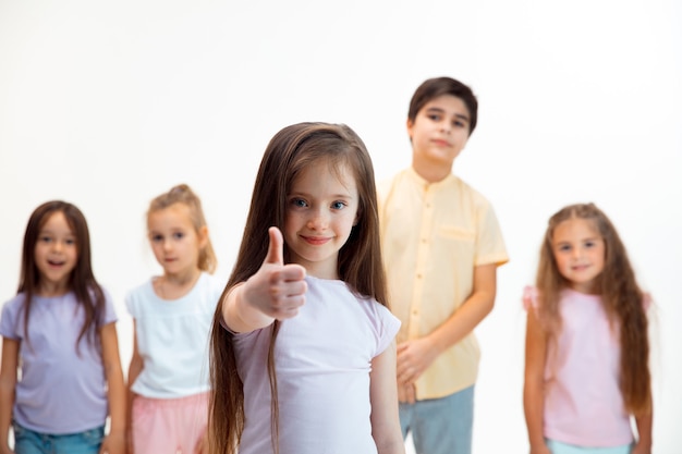 Foto gratuita el retrato de niño y niñas felices lindos niños pequeños en ropa casual elegante mirando al frente contra la pared blanca del estudio