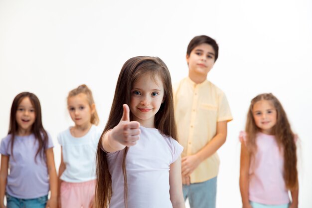 El retrato de niño y niñas felices lindos niños pequeños en ropa casual elegante mirando al frente contra la pared blanca del estudio